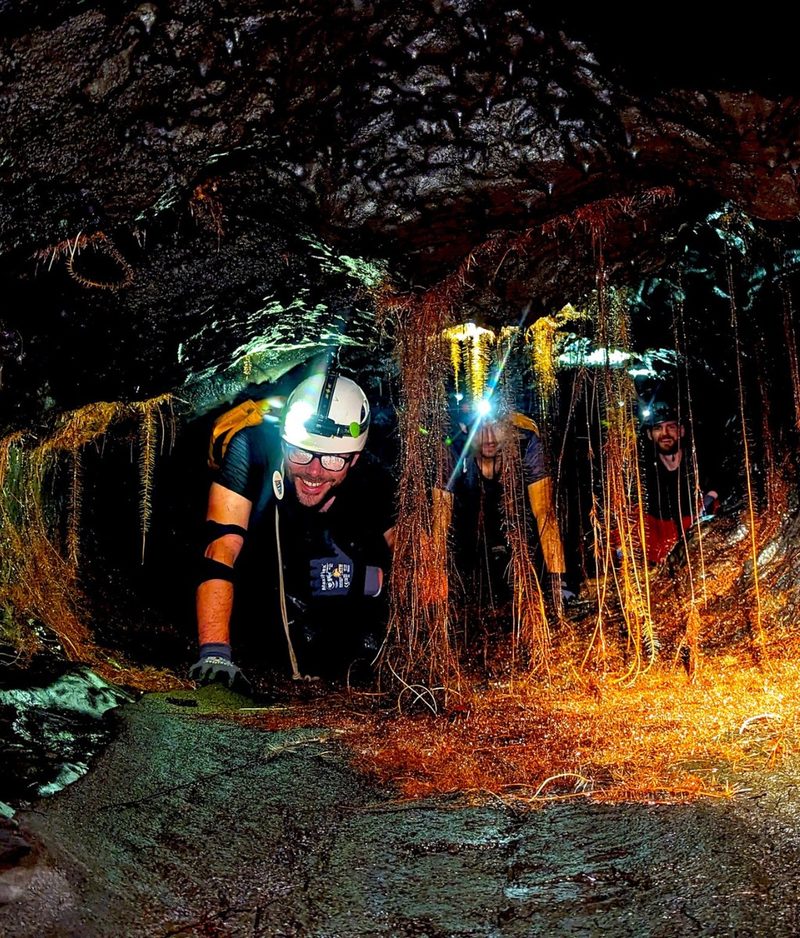 Un explorateur casqué, frontale allumée, entre les racines d'un tunnel